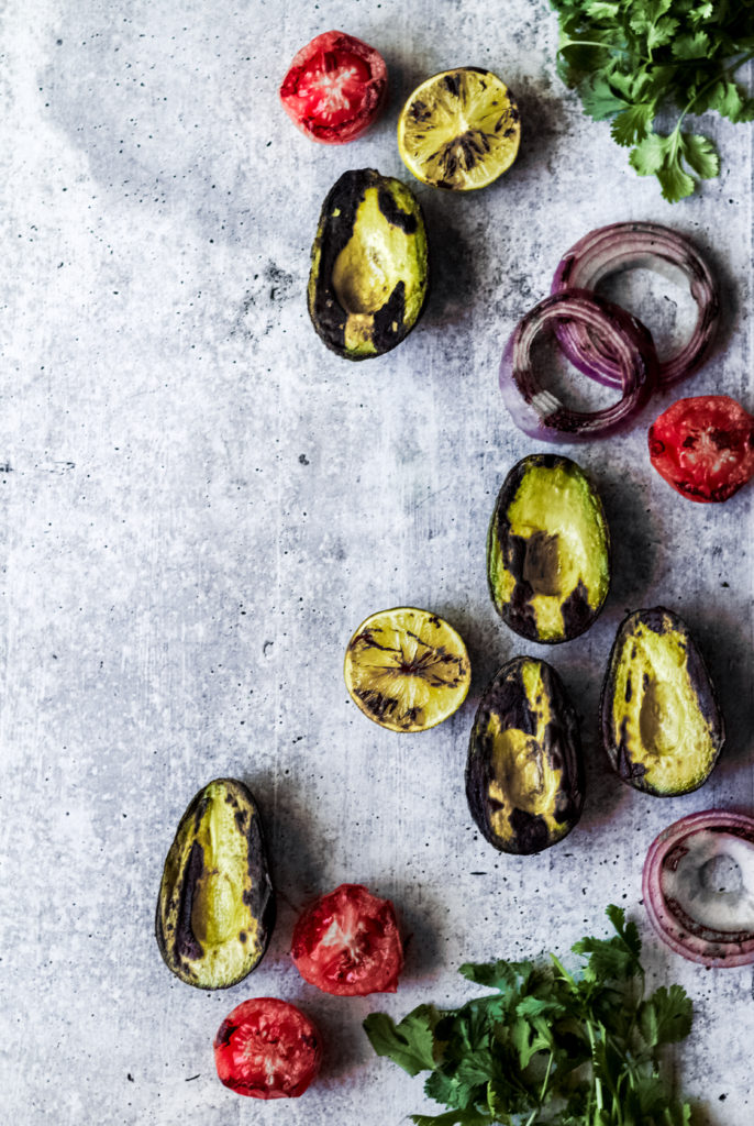 grilled sliced avocado halves, tomatoes, red onions and cilantro on a gray background