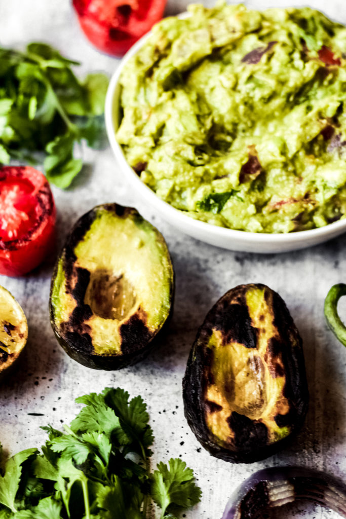 grilled vegan guacamole in a while bowl surrounded by grilled ingredients