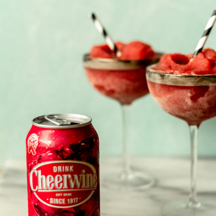 two cocktail glasses filled with cheerwine slush cocktails and a can of cheerwine soda