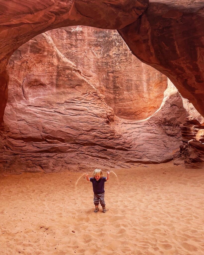 child throwing sand under sand dune arch