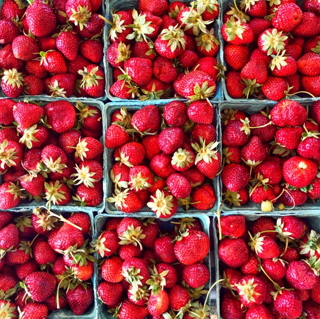 Close-up of several containers filled with ripe, red strawberries, some with green stems attached, arranged in a grid pattern.