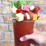 A hand holding a glass of food, showcasing creative bloody mary garnish ideas.