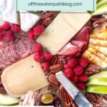 A charcuterie board with assorted cheeses, meats, pecans, raspberries, apple slices, and a small bowl of olives. Overlay text reads “Easy Charcuterie Board,” plus a step-by-step how to make a charcuterie board tutorial.