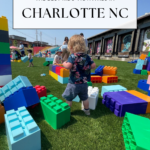A toddler plays on artificial grass surrounded by giant colorful building blocks at an outdoor activity area, with other children and adults in the background. Text overlay reads: Fun things to do in Charlotte with kids.