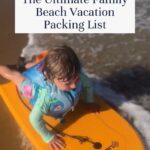 A young child wearing a blue life vest rides a yellow boogie board on shallow ocean waves, with water and sand visible—perfect inspiration for your family beach vacation packing list.