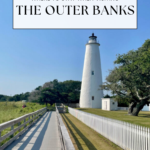 A tall white lighthouse stands beside a white picket fence and trees, with a wooden boardwalk leading toward it under a clear blue sky. Text reads: Where to stay when visiting Outer Banks towns.