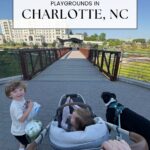 A person pushes a stroller with a toddler on a paved path, accompanied by a dog and another child holding a snack. They are on a bridge with charlotte parks and buildings visible in the background. Text at the top reads Best Family Friendly Parks & Playgrounds in Charlotte, NC.