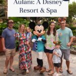 A group of five adults and two children pose with Mickey Mouse at Aulani, a Disney Resort & Spa, surrounded by lush greenery. Text overlay reads: “Aulani: A Disney Resort & Spa. Aulani review!”.
