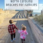Two young children walk hand in hand on a wooden boardwalk under a blue sky, heading to the shore. Text above reads A Guide to the Best North Carolina Beaches for Families.