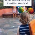 A young child wearing rainbow Mickey Mouse ears looks toward Disney characters and people in the background, with text above reading, Is the Aulani Character Breakfast worth it? Experience the magic of an Aulani character breakfast firsthand.