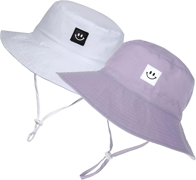 Two bucket hats with chin straps, one white and one light purple, each featuring a square patch with a simple black-and-white smiley face design on the front.
