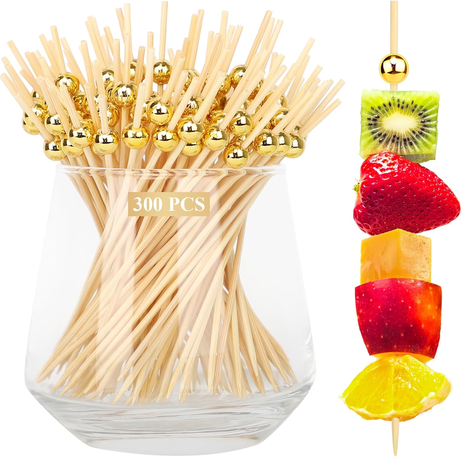 A glass container holds a bundle of bamboo cocktail picks with gold beads on top. Next to it, a skewer displays stacked fruit pieces: kiwi, strawberry, mango, apple, and orange. A label reads 300 PCS.