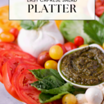 A caprese salad platter with sliced tomatoes, mozzarella balls, basil leaves, yellow and red cherry tomatoes, and a small bowl of pesto. The text reads Easy Caprese Salad Platter.