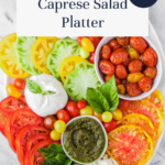 Colorful Caprese salad platter with heirloom tomatoes, mozzarella, roasted tomatoes, pesto, basil, and yellow cherry tomatoes on a white oval plate. Text reads “Fresh Flavor Caprese Salad Platter.”.