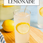 A glass of lemonade with a lemon slice and two straws sits on a wooden board. A whole lemon, a pitcher of lemonade, and a striped towel are nearby. Text reads: 3 Ingredients Fresh Lemonade..