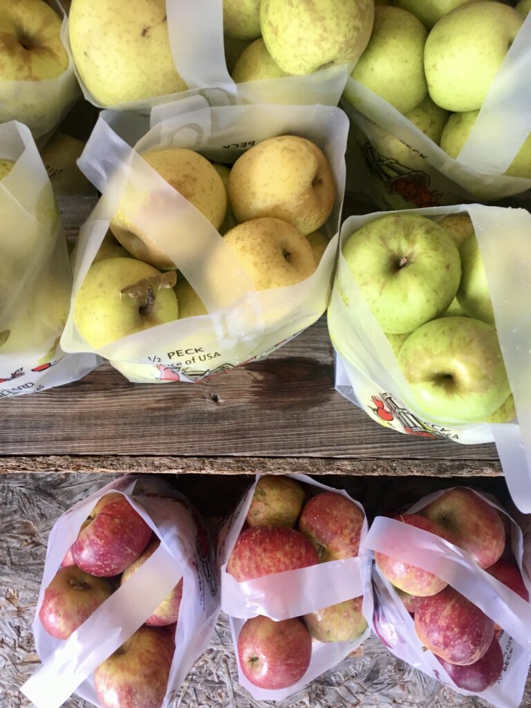 Bags of apples in varying shades of yellow, green, and red are arranged on a wooden surface, viewed from above.
