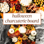 Charcuterie board with cheese, deli meats, crackers, olives, nuts, pumpkins, skull decor, flowers, and Halloween candy on a dark tray, with spider web decorations and Halloween charcuterie board text.
